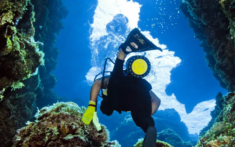 A scuba diver swimming through a narrow underwater rock passage toward the surface